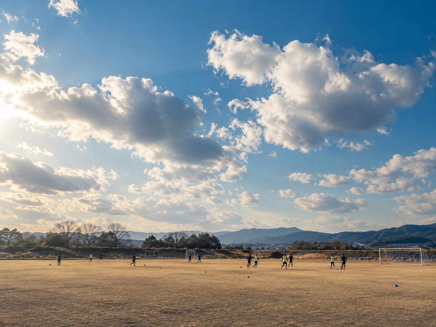 広い空の下のサッカー練習場。遠くに小さく選手。個人は特定できない。
